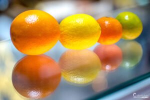 Agrumes colorés en équilibre sur une surface réfléchissante, illustrant des jeux subtils de lumière et l'éclat vibrant des fruits.