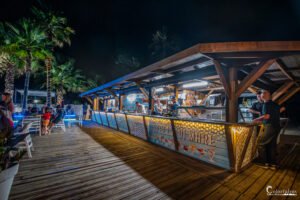 Soirée festive estivale dans un bar en bord de mer, éclairé sous des palmiers, idéal pour échapper à l'ordinaire et profiter de l'ambiance de vacances.