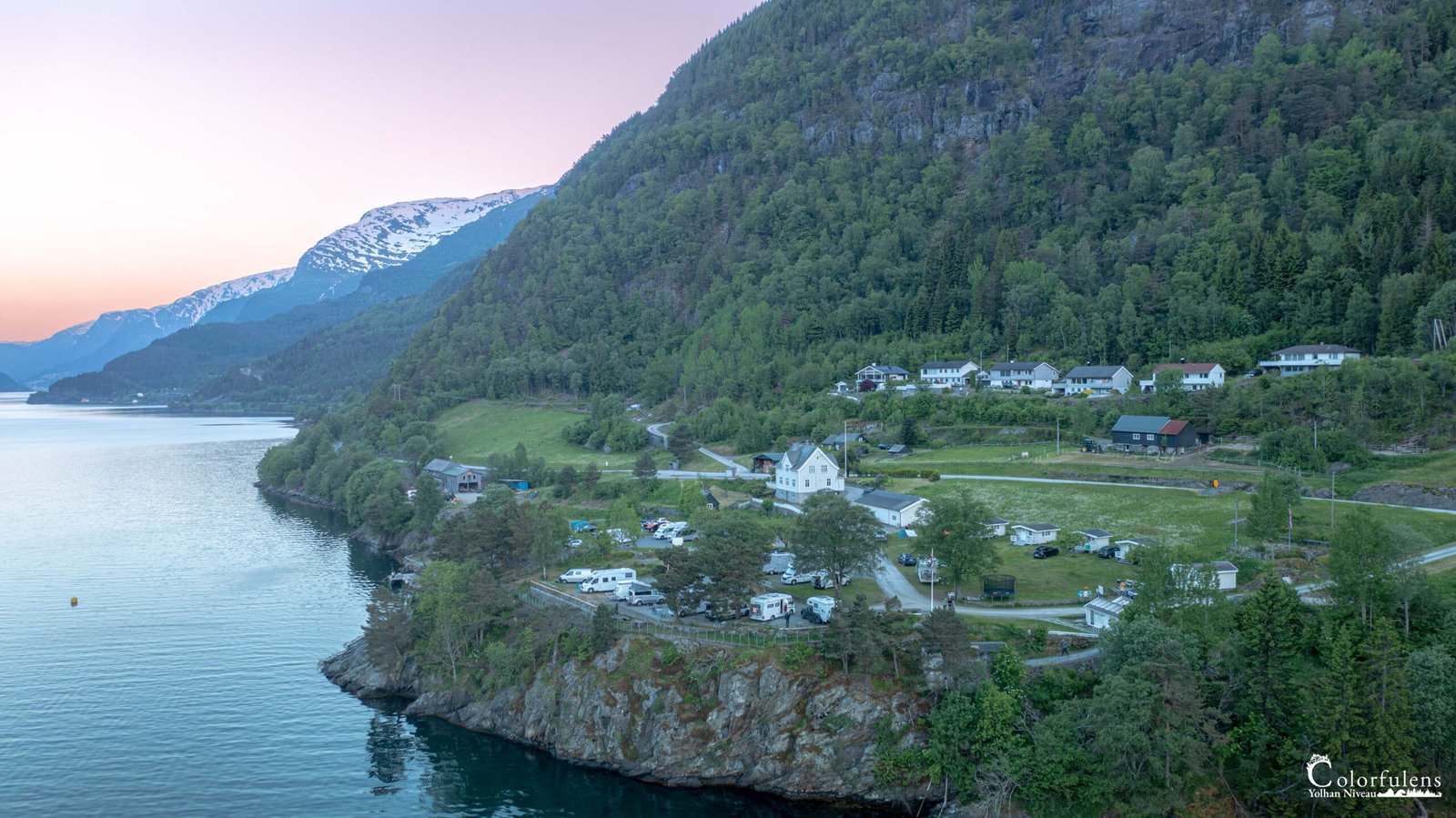 Ce camping norvégien capté au crépuscule incarne tranquillité et beauté sauvage, avec ses roulottes et chalets nichés entre lac et montagnes enneigées.