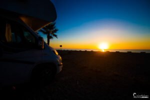 Coucher de soleil magnifique avec un camping-car sur la plage, illustrant la liberté et l'évasion au cœur de la nature.