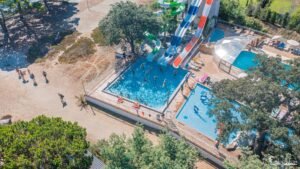 Vue aérienne captivant l'ambiance enjouée du Camping Merendella en Corse, où le bleu des piscines et le vert de la nature environnante offrent une oasis de détente estivale.