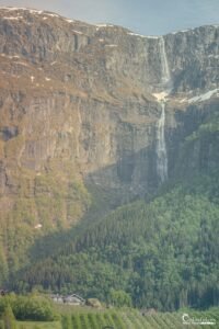 Photographie immersive d'une cascade impressionnante en pleine montagne, avec une maison isolée nichée dans la forêt, parfaite pour échapper au quotidien.