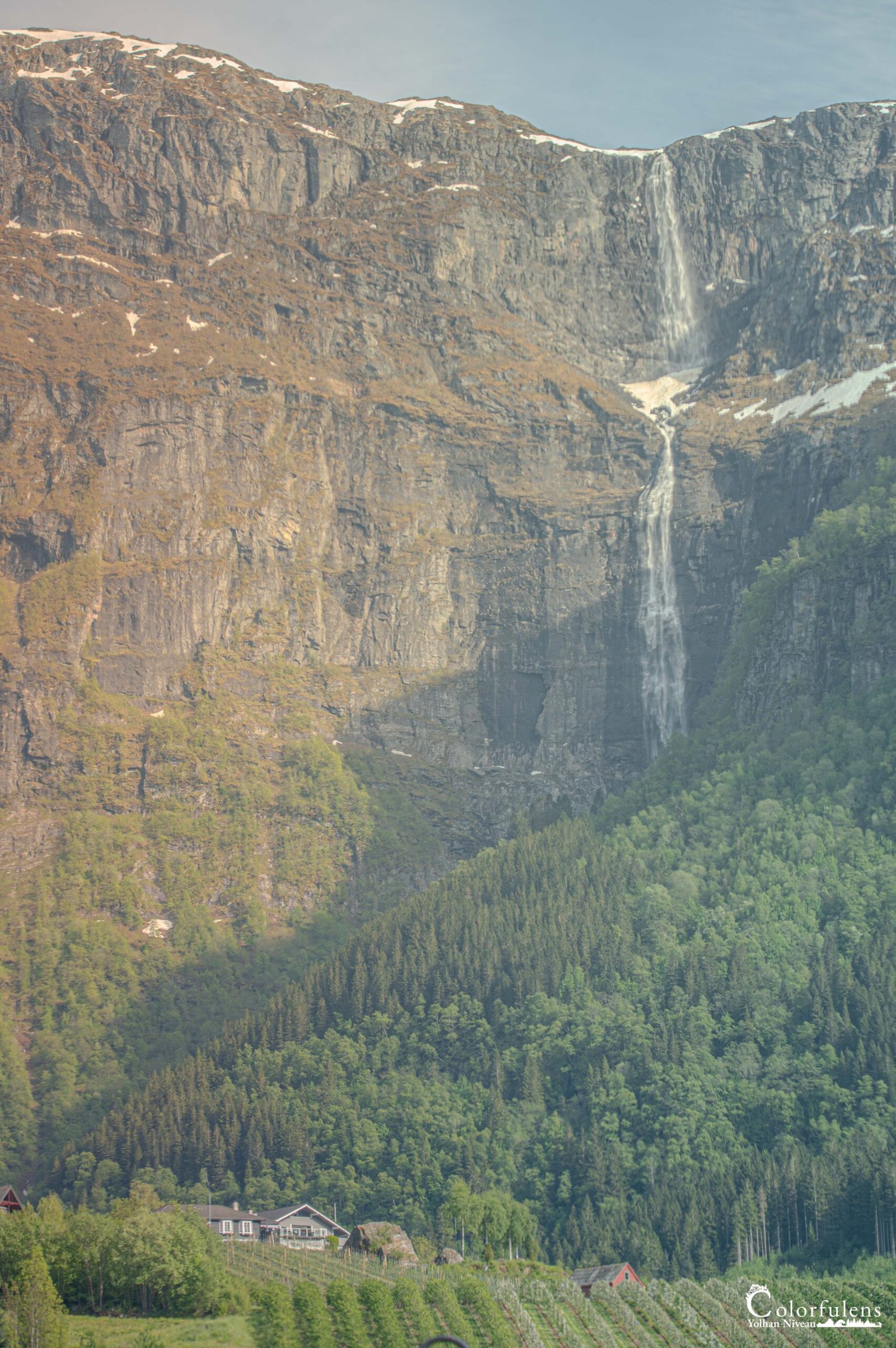 Photographie immersive d'une cascade impressionnante en pleine montagne, avec une maison isolée nichée dans la forêt, parfaite pour échapper au quotidien.