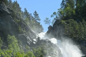 Cascade majestueuse en Norvège plongeant dans la brume avec une forêt en toile de fond, capturant la puissance et la sérénité de la nature.