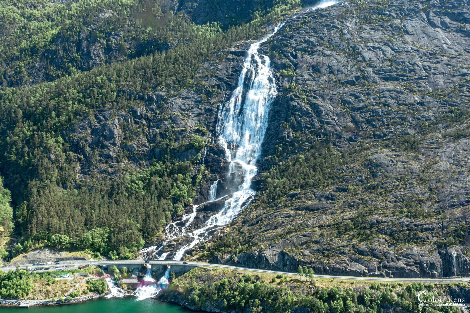 Photo de cascade spectaculaire dans une montagne verdoyante avec un pont en arc, montrant la tranquillité et la puissance de la nature.