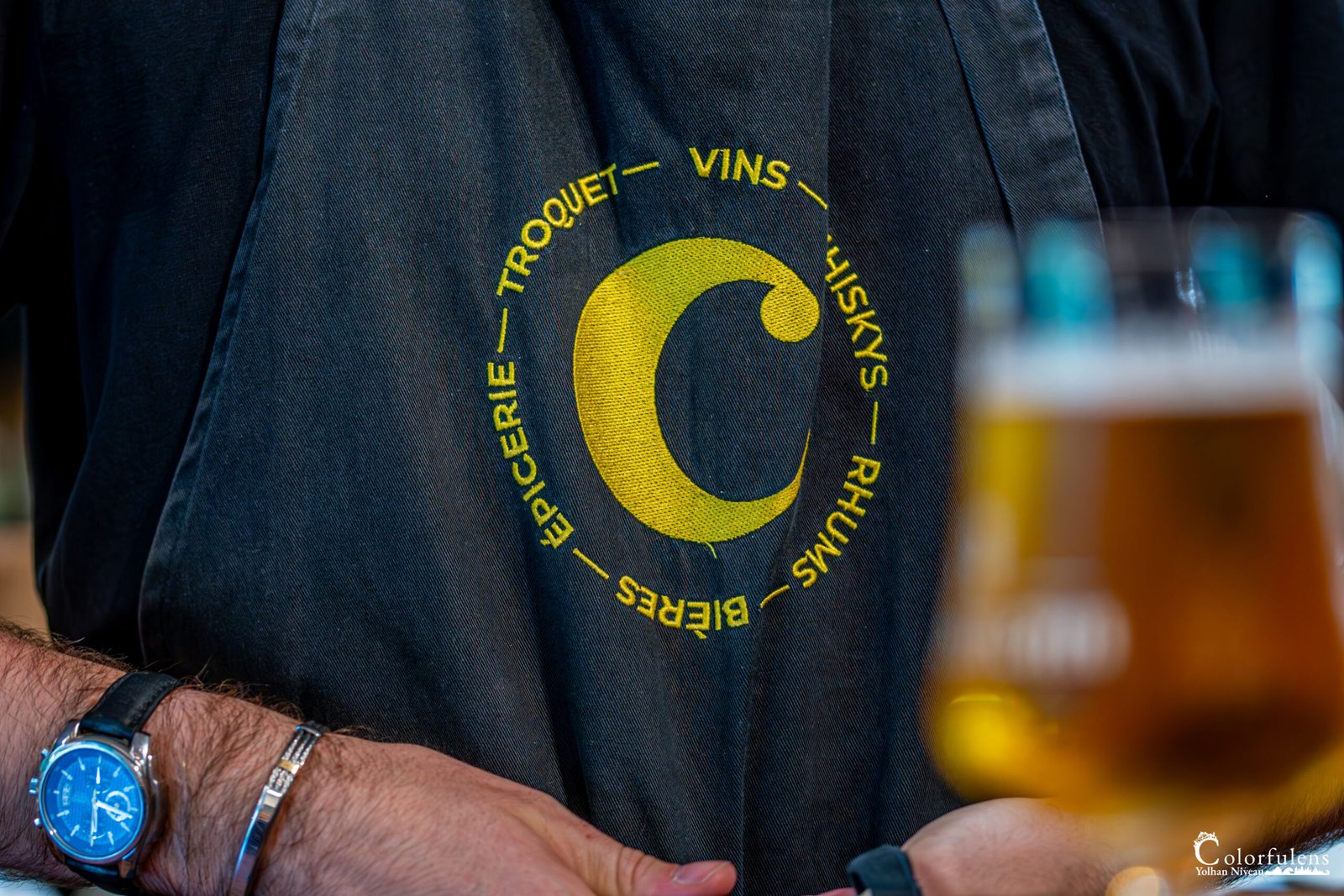 Sommelier en tablier noir tenant un verre de bière artisanale dans une épicerie fine à Muzillac, dépeignant la convivialité et la qualité des produits.