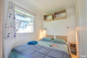 Chambre confortable en bois dans le camping Merendella, Corse, avec un lit douillet, une lampe de chevet allumée, et des livres pour une atmosphère de détente.