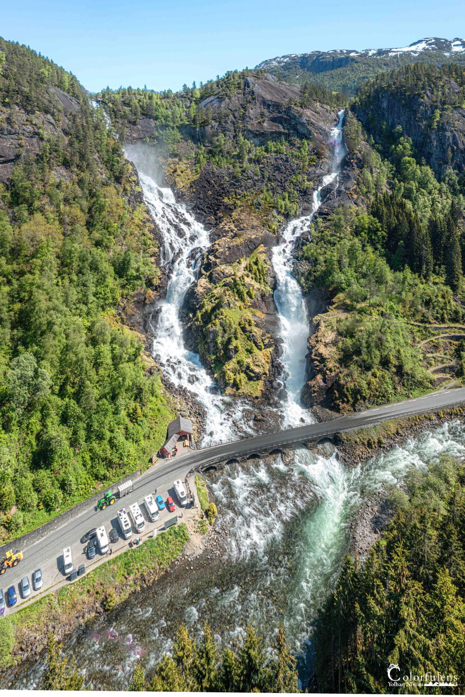 Photo impressionnante d'une chute d'eau énergique en Norvège, entourée d'un paysage verdoyant et contrastant avec le calme environnant.