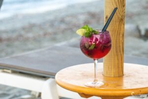 Cocktail violet agrémenté de fruits rouges et de menthe fraîche, posé sur une table de plage pour des moments de détente en duo.