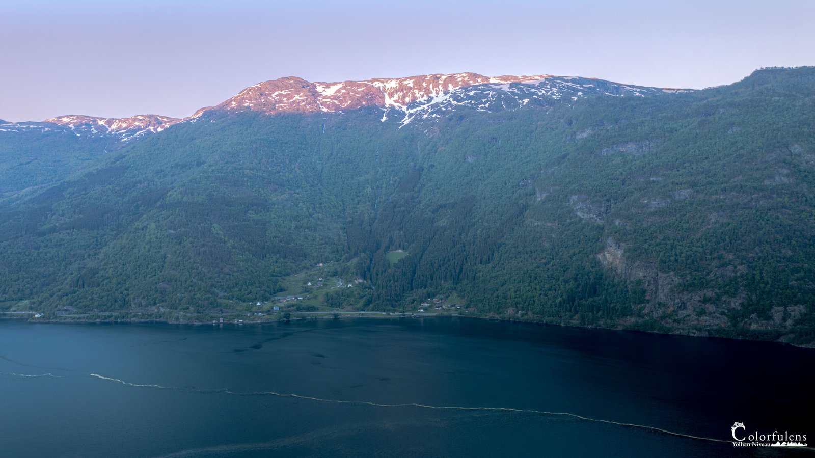 Paysage de coucher de soleil sur le Hardangerfjord en Norvège avec montagnes enneigées et forêt.