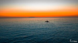 Un pêcheur en parfaite harmonie avec l'océan, capturé dans un moment de tranquillité absolue, le ciel se parant de teintes vespérales apaisantes.