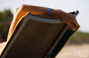 Une main ferme enlaçant une chaise longue, avec un bracelet "Merendella 2022" symbolisant des vacances relaxantes en Corse.