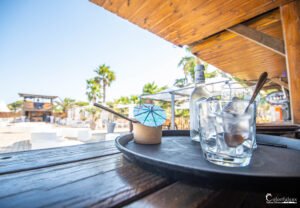 Détente sous le soleil corse sur une terrasse du camping Merendella, entourée de palmiers et d'une ambiance conviviale, avec un verre d'Orezza pour se rafraîchir.