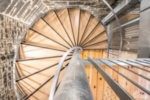 Escalier moderne en colimaçon intégrant bois clair et pierre brute avec éclairage naturel.