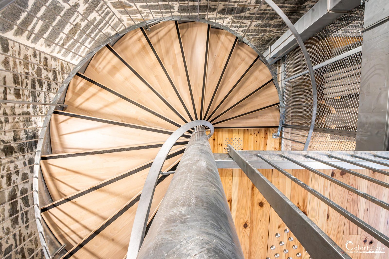 Escalier moderne en colimaçon intégrant bois clair et pierre brute avec éclairage naturel.
