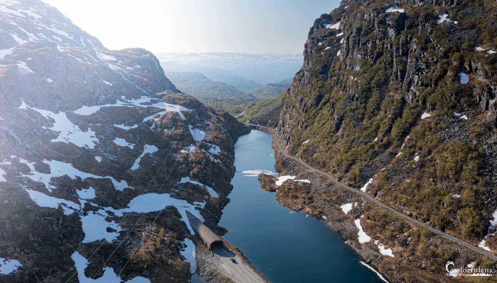 Vue panoramique d'une route sinueuse traversant des montagnes enneigées et longeant un fjord en Norvège, illustrant l'harmonie entre nature et technologie humaine.