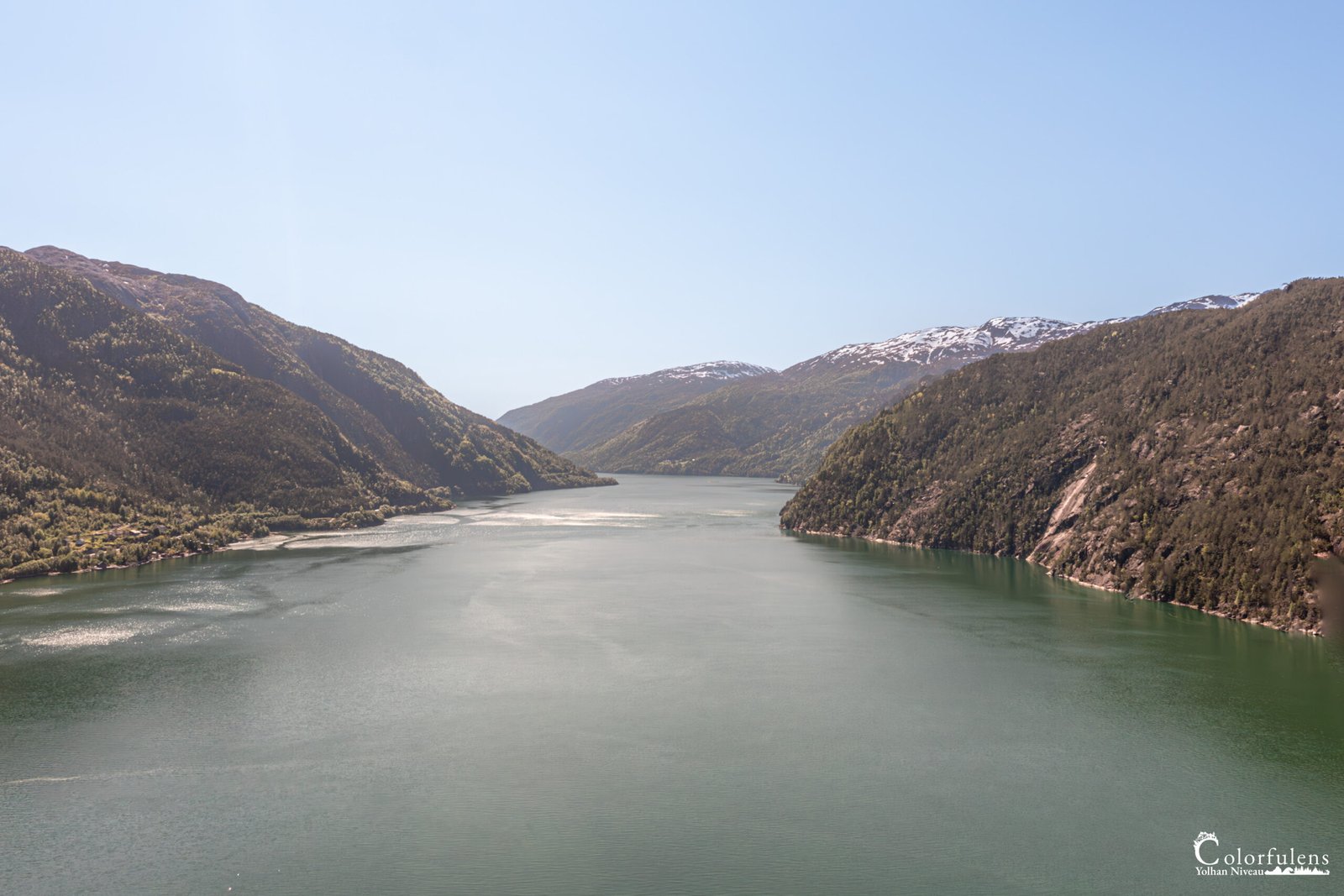 Panorama serein d'un fjord norvégien aux eaux claires reflétant les montagnes enneigées, offrant une escapade visuelle et une invitation à l'exploration.