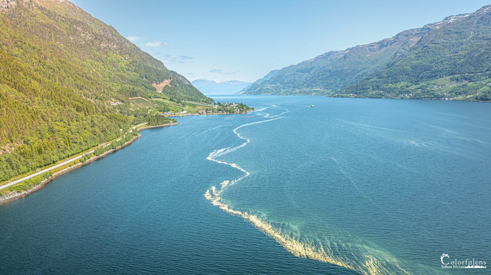 Fjord norvégien en été avec montagnes escarpées et sillage de bateau, capturant la quiétude et majesté du paysage naturel.