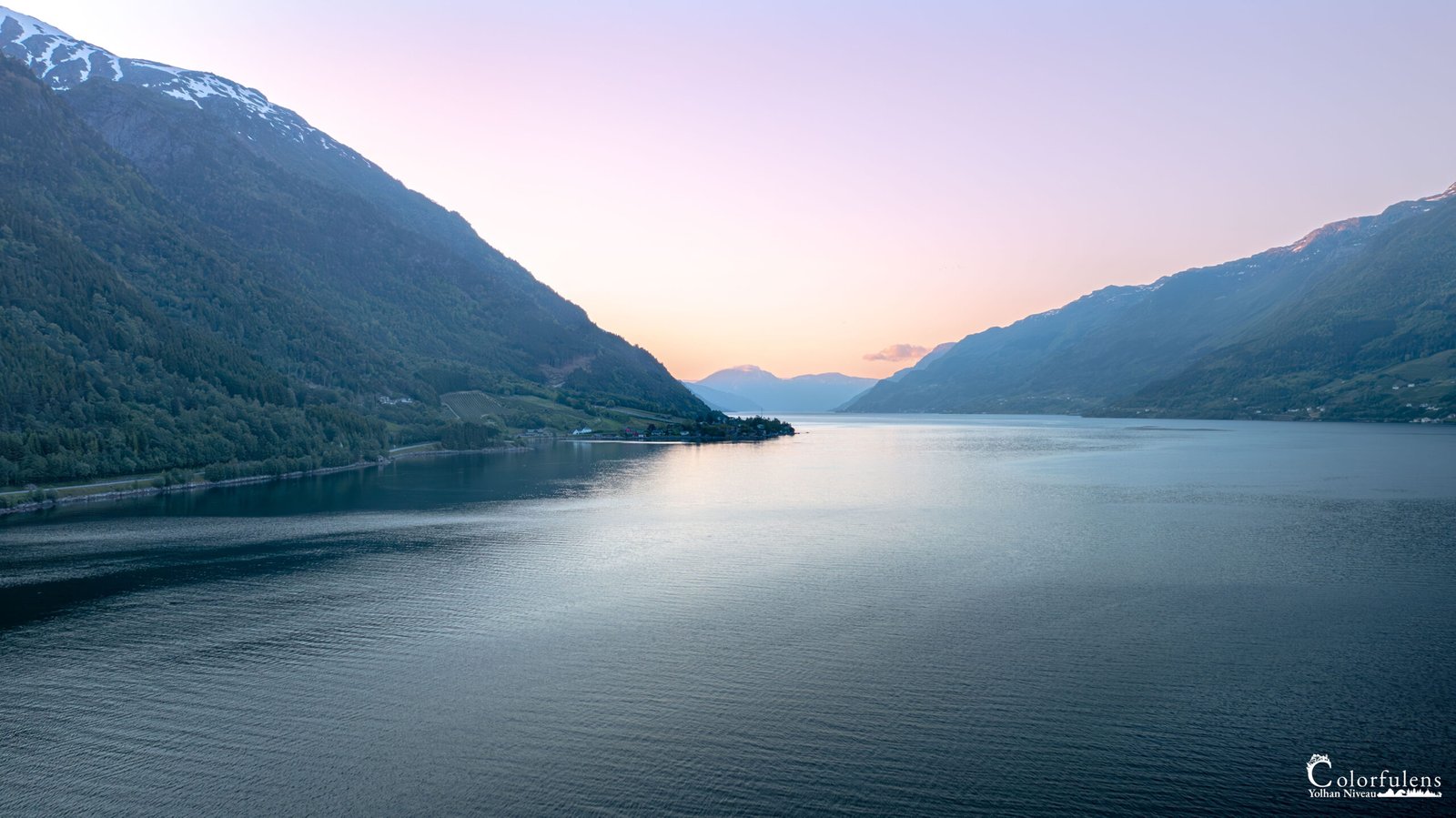 Vue panoramique du fjord norvégien au crépuscule, entre montagnes imposantes et eaux calmes.