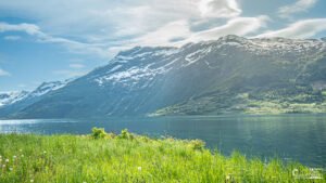 Fjord norvégien avec montagnes enneigées se reflétant dans des eaux claires sous la lumière estivale, capturant l'harmonie entre la nature et la présence humaine.