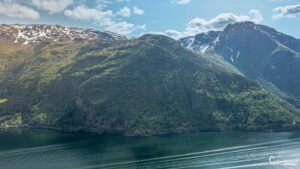 Vue apaisante du Hardangerfjord en Norvège, où les eaux calmes reflètent les montagnes enneigées, créant un miroir naturel et une ambiance sereine.