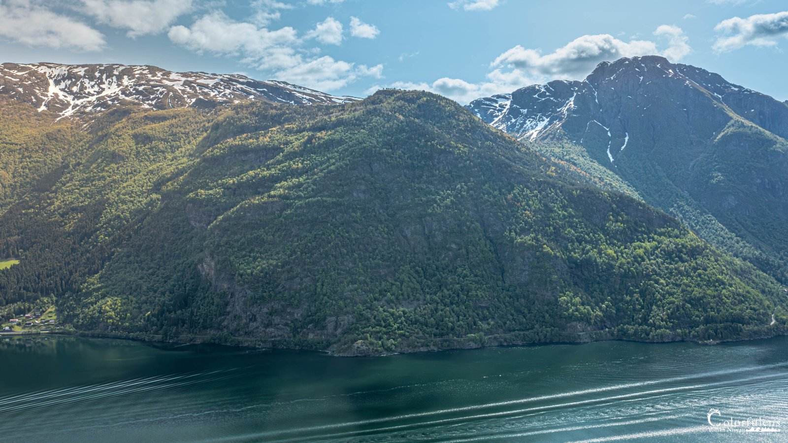 Vue apaisante du Hardangerfjord en Norvège, où les eaux calmes reflètent les montagnes enneigées, créant un miroir naturel et une ambiance sereine.