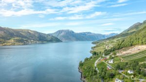 Une image de fjord norvégien avec des montagnes ensoleillées et un village pittoresque surplombant l'eau cristalline.