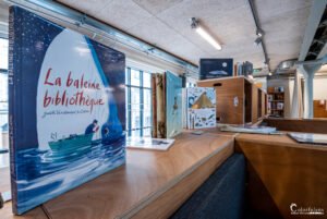 Baleine portant un bateau rempli de livres et l'atmosphère chaleureuse d'une bibliothèque pour enfants, incitant à l'éveil littéraire.