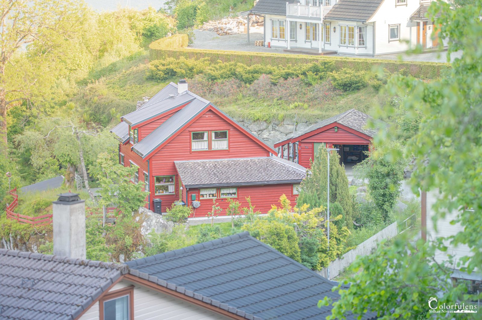 Maison rouge nichée dans la nature, entourée de verdure luxuriante et dotée de toits de tuiles sombres, dépeignant une vie paisible à la campagne.