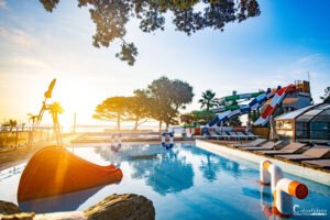 Une ambiance matinale paisible au camping Merendella en Corse avec piscine et toboggans éclairés par un soleil naissant, promesse de divertissement et détente.