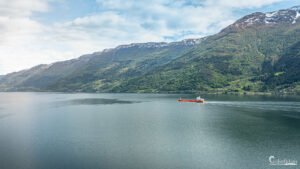 Vue du fjord norvégien avec bateau orange sur eaux calmes reflétant montagnes verdoyantes et sommets enneigés