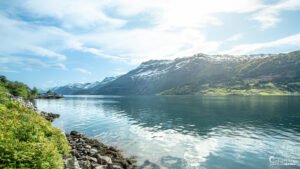 Vue panoramique du Hardangerfjord en Norvège avec montagnes enneigées et reflets dans l'eau, symbolisant la paix et la tranquillité.