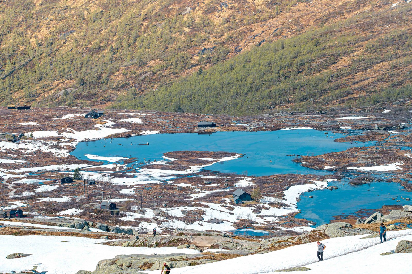 Paysage hivernal scandinave avec lac gelé, cabanes en bois et montagnes enneigées sous ciel clair.