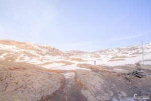 Scène pittoresque de randonneurs sur un chemin montagneux enneigé malgré l'été, avec un ciel bleu en toile de fond.