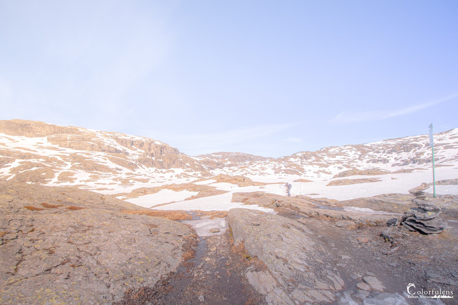 Scène pittoresque de randonneurs sur un chemin montagneux enneigé malgré l'été, avec un ciel bleu en toile de fond.
