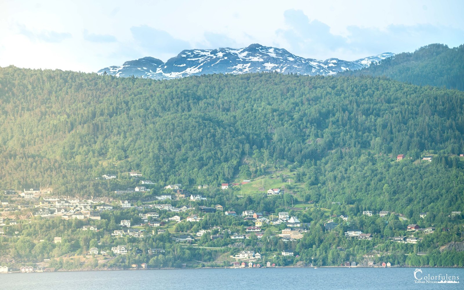 Paysage féerique d'un fjord norvégien entouré de montagnes enneigées et de forêts verdoyantes.