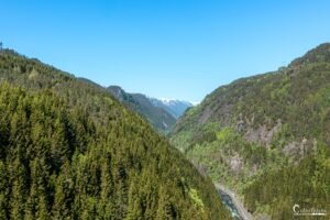 Paysage de montagnes verdoyantes entourant une vallée encaissée, ciel bleu clair en arrière-plan
