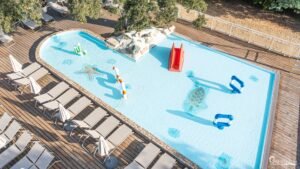 Vue aérienne d'une piscine ensoleillée au camping Merendella, Corse, entourée de chaises longues, idéale pour des vacances de détente et jeux aquatiques.