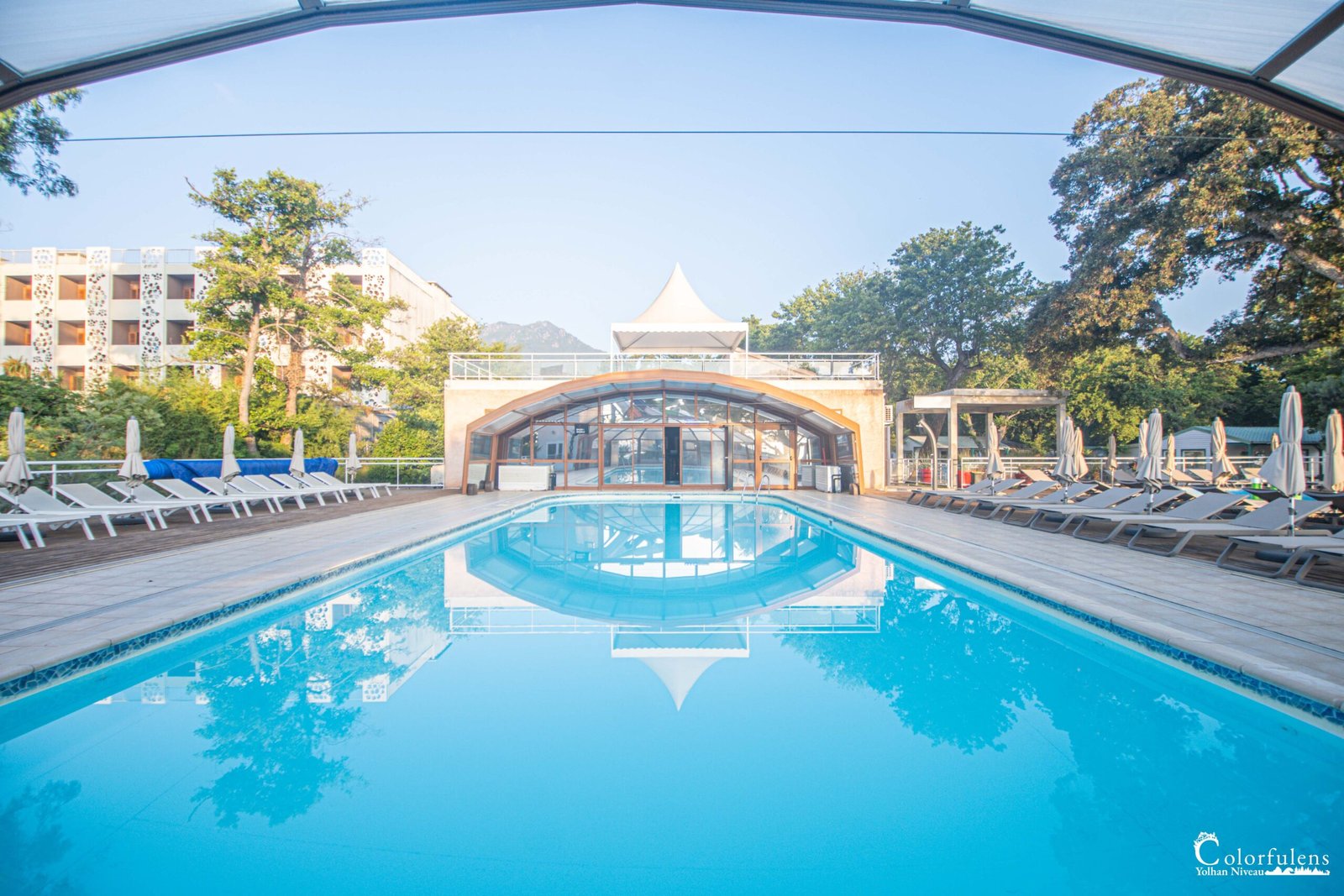 Hôtel de luxe en Corse avec piscine, reflet du ciel et des montagnes, pour une expérience de détente et de sérénité.