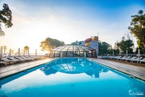 Piscine luxueuse en Corse au lever du soleil, entourée de palmiers et de transats, offrant détente, calme et vue idyllique.