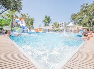 Image d'une piscine animée en été, montrant des familles profitant de toboggans aquatiques sous le soleil.