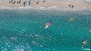 Vue aérienne de kayakistes profitant des eaux turquoise et du sable fin de Corse, symboles de détente et de beauté naturelle.