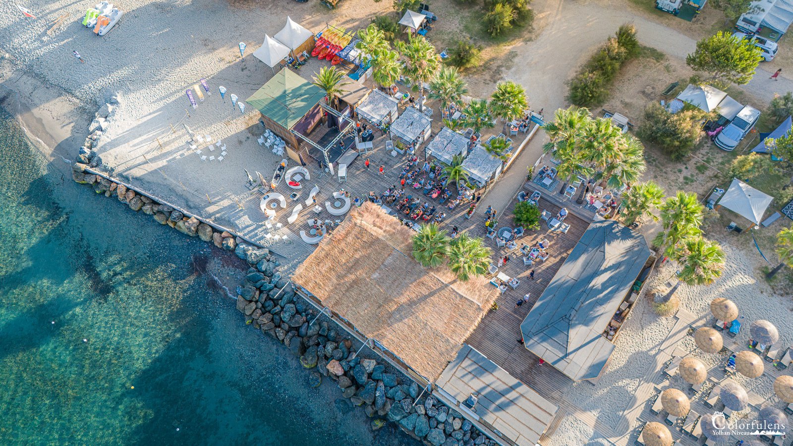 Vue aérienne du camping de Merendella en Corse, offrant détente en bord de mer avec plages, parasols, et activités estivales.