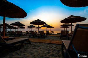 Silhouettes de parasols de paille se dessinant sur une plage déserte au crépuscule, offrant un spectacle de tranquillité et de beauté naturelle.