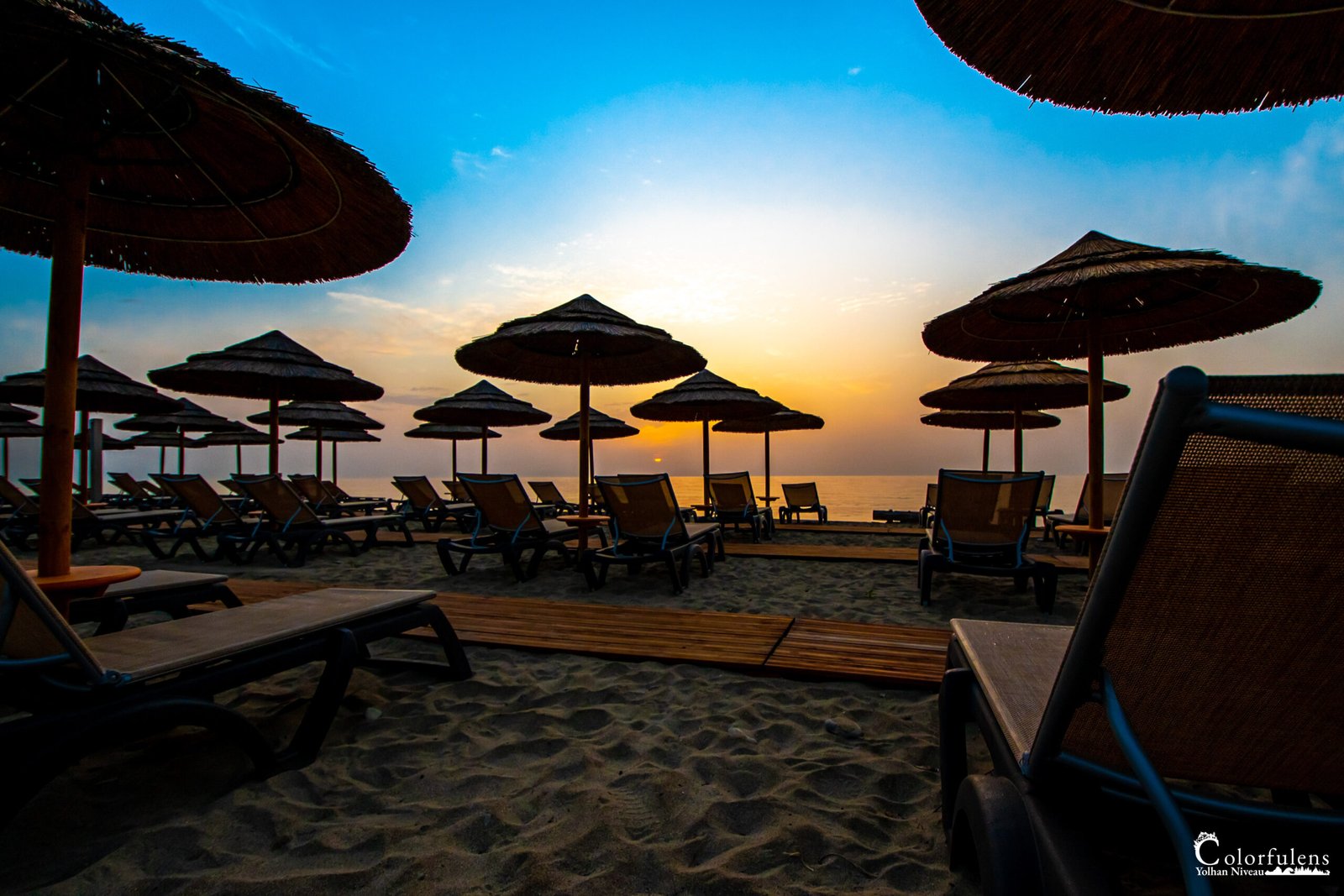 Silhouettes de parasols de paille se dessinant sur une plage déserte au crépuscule, offrant un spectacle de tranquillité et de beauté naturelle.