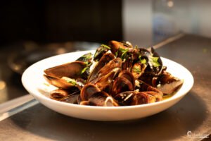 Assiette de moules à la provençale, décorée d'herbes aromatiques, baignée dans une lumière douce soulignant leur fraîcheur gourmande.