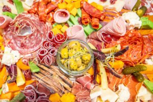 Photo d'un plateau coloré de charcuterie et fromage avec des cornichons, jambon serrano, saucisson, et fromages divers, idéale pour des moments de partage et de gourmandise.