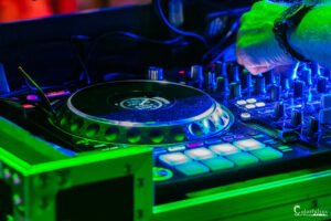 Photographie captivante d'une platine DJ sous un éclairage néon vert et bleu en club, soulignant l'énergie de la musique.