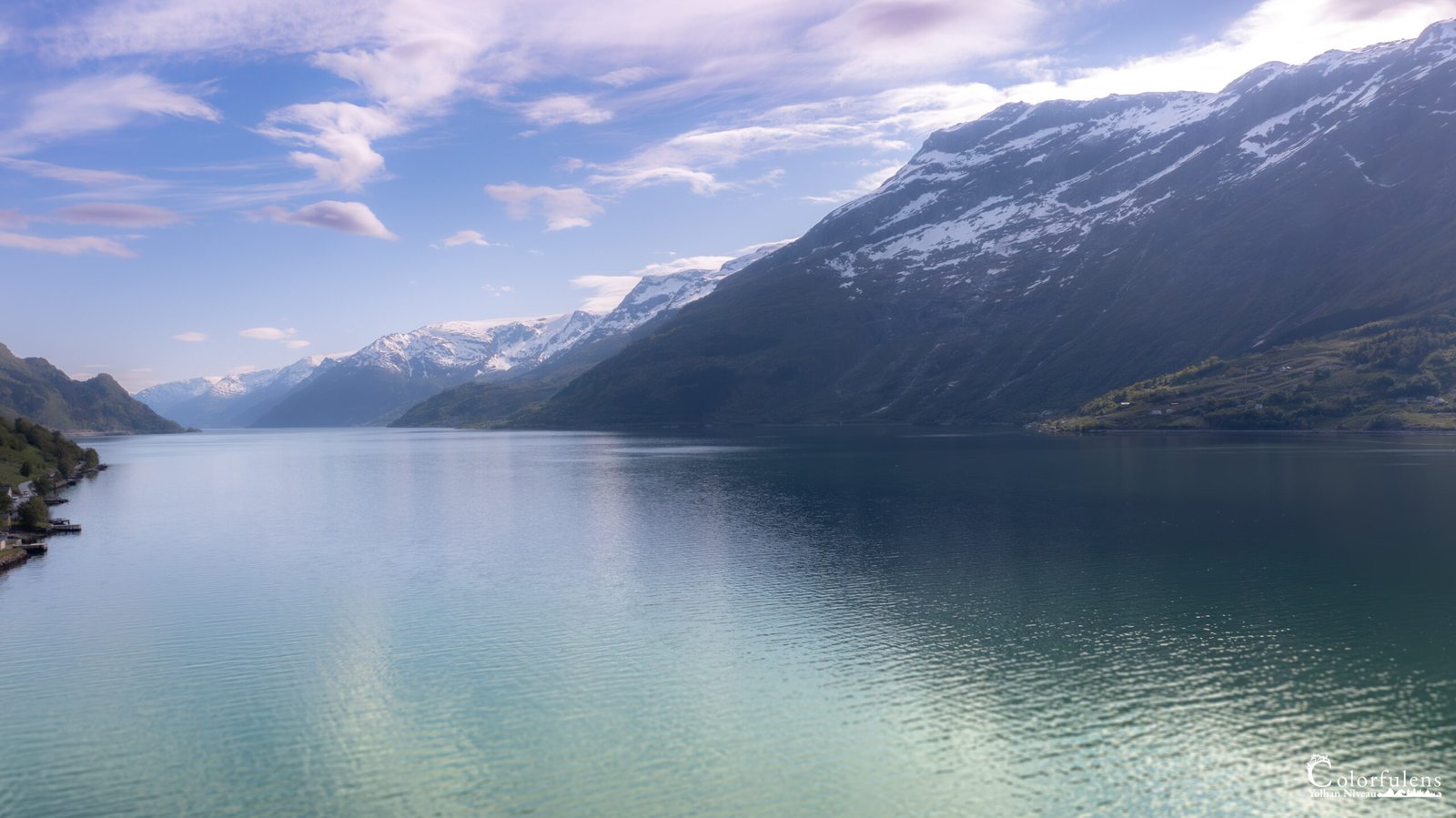 Reflets miroitants des montagnes enneigées dans les eaux du Hardangerfjord, témoignant de la majestueuse tranquillité de la nature norvégienne.