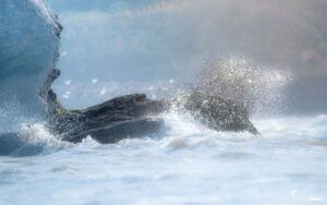 Vagues puissantes frappant des rochers sous la lumière du soleil, créant des éclaboussures étincelantes.